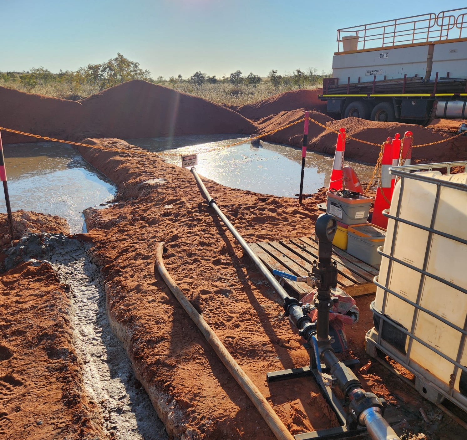 Mud pits beside a drill rig on red dirt